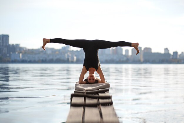 Esercizio di yoga di pratica della giovane donna al pilastro di legno calmo