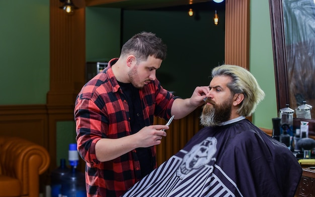 Esigi te stesso uomo maturo dal parrucchiere La cura dei capelli e il concetto di toelettatura maschile ottengono una forma perfetta uomo barbuto che si fa tagliare la barba dal barbiere baffi e barba seduti sulla sedia dal parrucchiere