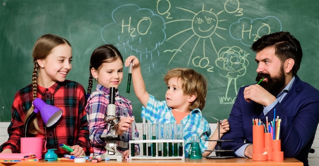 Esperimento di chimica scolastica Spiegare la chimica ai bambini Affascinante lezione di chimica Insegnante uomo barbuto e alunni con provette in classe Laboratorio di chimica della scuola La scienza coinvolge la teoria