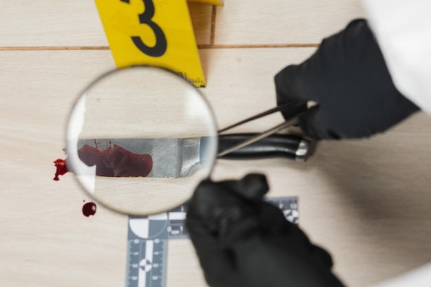 Esperto criminologico attraverso una lente d'ingrandimento che guarda un coltello insanguinato sulla scena del crimine