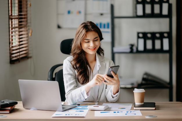 Esperto di business sicuro attraente giovane donna sorridente digitando laptop ang tenendo tablet digitale sulla scrivania in officexA