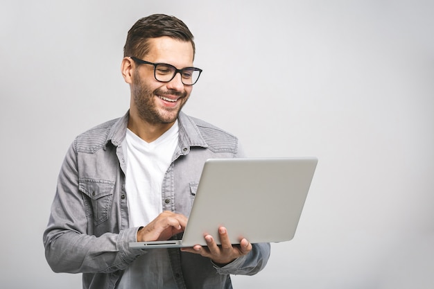 Esperto in affari sicuri. Giovane uomo bello sicuro in computer portatile della tenuta della camicia e sorridere mentre stando contro il fondo bianco