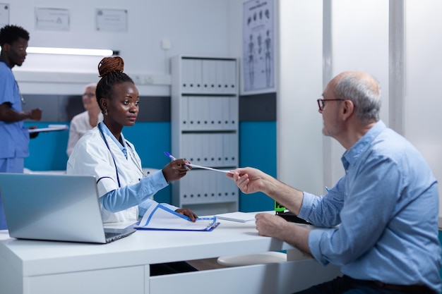 Esperto medico sanitario che consegna i documenti di dimissione a un paziente in pensione sano mentre parla degli effetti collaterali del trattamento. Specialista del medico generico che discute con l'anziano sul procedimento medico