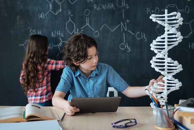 Esplorare la scienza insieme. Curiosi adolescenti capaci coinvolti seduti a scuola e godendo di lezioni di chimica mentre scrivevano sulla lavagna e utilizzavano tablet