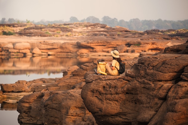 Esploratore asiatico della donna che si siede sulla scogliera della roccia con guardando la mappa cartacea nel grand canyon di Sam Phan Bok della Thailandia