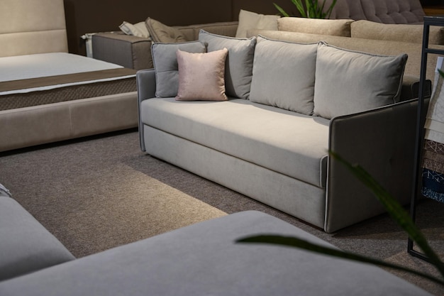 Esposizione di divano imbottito elegante e confortevole grigio chiaro con cuscini rosa vicino a un supporto con campioni e campioni di tessuto di diverse trame e qualità Showroom negozio di mobili