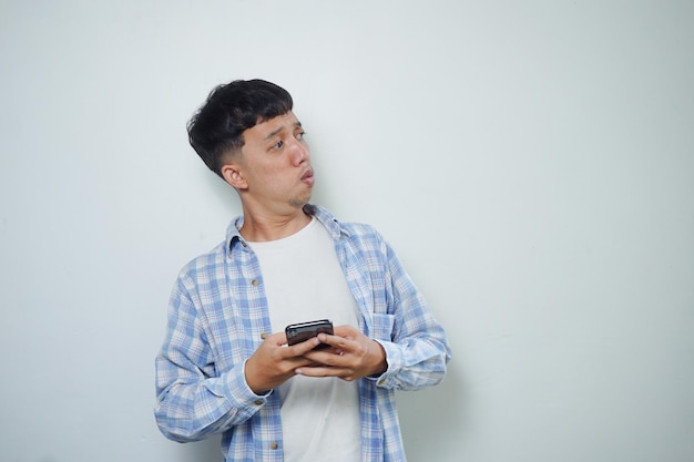 Espressione facciale dell'uomo asiatico che guarda lateralmente tenendo il telefono cellulare isolato su sfondo bianco