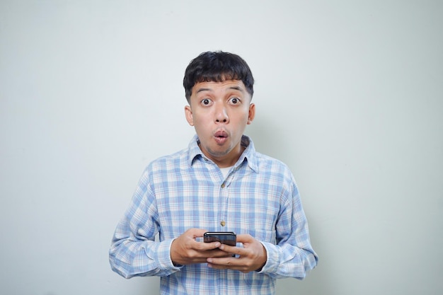 Espressione facciale sorpresa dell'uomo asiatico che guarda l'obbiettivo utilizzando lo smartphone
