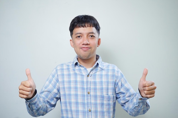 Espressione facciale sorridente dell'uomo asiatico che mostra entrambi i pollici alla macchina fotografica