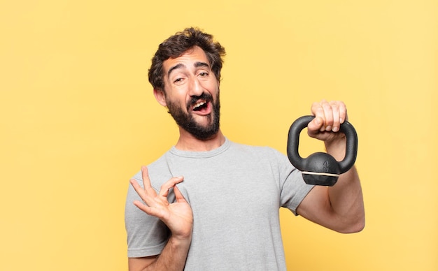 Espressione felice del giovane atleta barbuto pazzo e che tiene un dumbbell