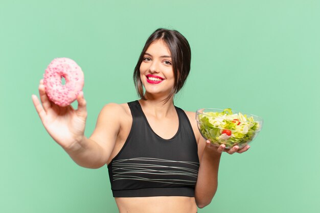 Espressione felice della giovane donna graziosa di sport e che tiene un'insalata