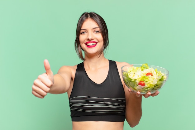 Espressione felice della giovane donna graziosa di sport e che tiene un'insalata