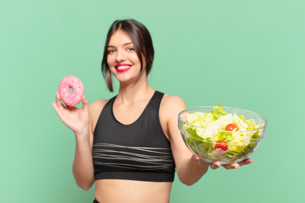 Espressione felice della giovane donna graziosa di sport e che tiene un'insalata