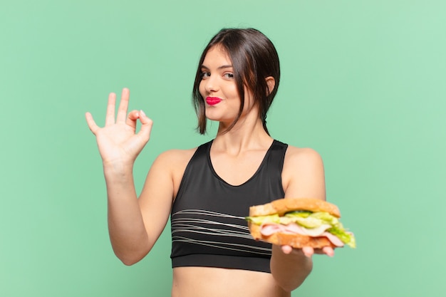 Espressione felice della giovane donna graziosa di sport e che tiene un panino