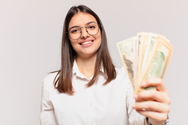 Espressione felice della giovane donna graziosa e che tiene le banconote del dollaro?