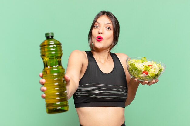 Espressione sorpresa di giovane bella donna sportiva e con in mano un'insalata