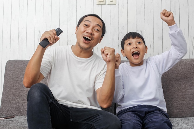 Espressioni eccitate di padre e figlio che guardano la televisione alla loro squadra di calcio preferita che fanno a