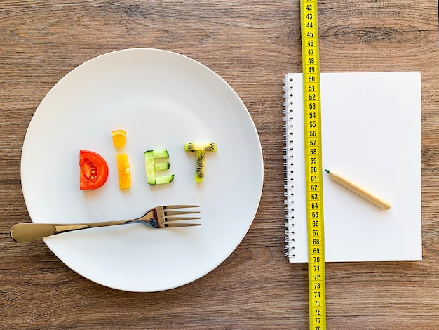 Esprima la DIETA fatta delle verdure affettate in piatto bianco e nel piano di dieta su legno