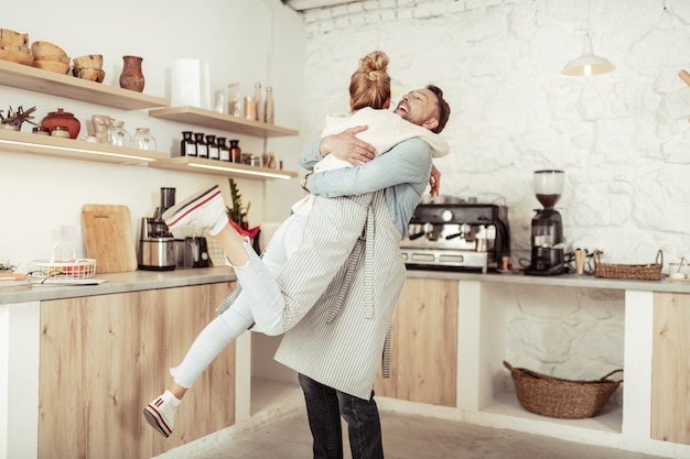 Essere contento. Gioiosa coppia sposata che si abbraccia nel mezzo della loro spaziosa cucina.