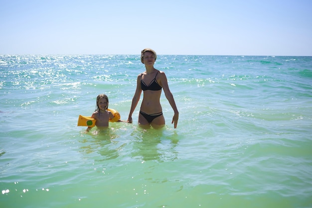 Estate famiglia felice di sei anni bambino biondo che gioca e salta le onde d'acqua che abbraccia la madre della donna nella spiaggia della riva del mare