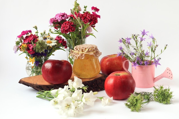 Estate natura morta mazzi di fiori selvatici in vari vasi mele e un barattolo di marmellata su una sega in legno sfondo chiaro primo piano