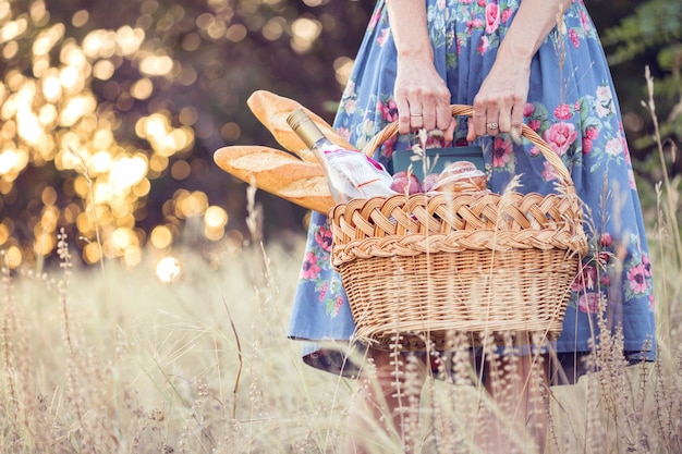 Estate - picnic nel prato. ragazza con in mano un cestino per un picnic con baguette, vino, bicchieri, uva e panini