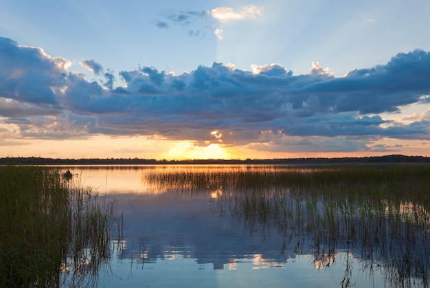 Estate rushy vista del tramonto sul lago con riflessi di nuvole nella superficie dell'acqua e barca con fisher