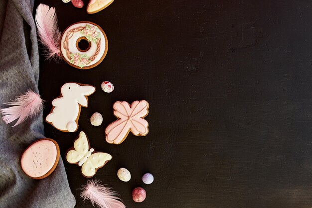 Estetica pasquale primaverile con biscotti decorati piume su sfondo nero spazio copia piatto banner di Pasqua