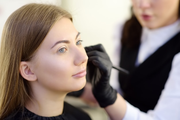 Estetista che applica il tono della fondazione usando il pennello speciale sul viso giovane e bella modella. Cura del viso e trucco