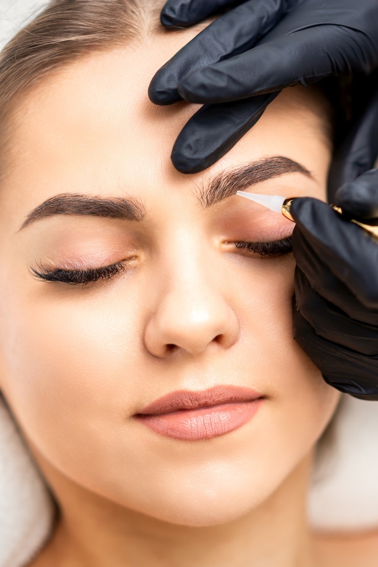 Foto estetista che applica trucco permanente sulle sopracciglia di giovane donna con una speciale macchina utensile per tatuaggi