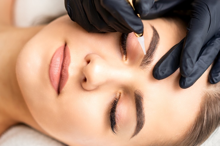 Foto estetista che applica trucco permanente sulle sopracciglia di giovane donna con una speciale macchina utensile per tatuaggi