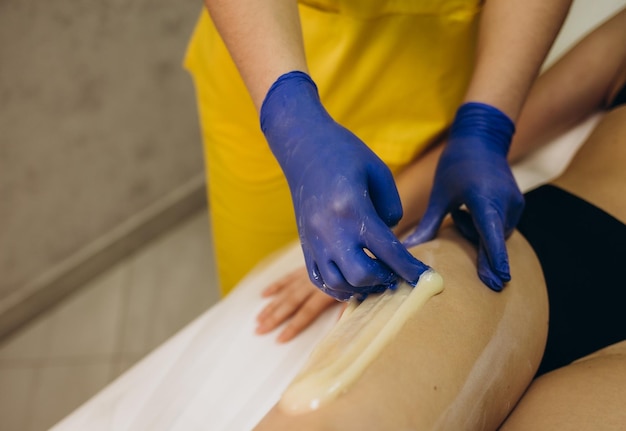 Estetista che depila le gambe della giovane donna con zucchero liquido nel centro termale