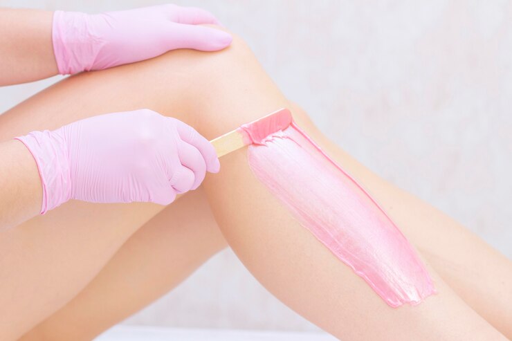 Estetista che depura le gambe di una giovane donna con cera rosa in un centro termale