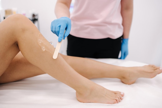 Estetista donna in bagliori blu applica il gel di contatto sulla gamba di una donna per la depilazione laser in studio di cosmetologia Primo piano