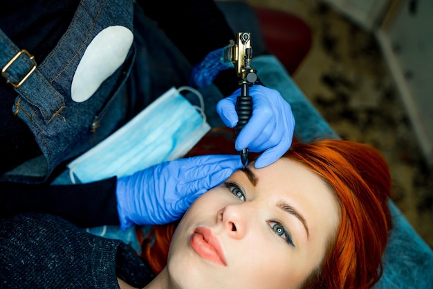 Estetista professionista che fa il tatuaggio del sopracciglio sul viso della donna Trucco permanente del sopracciglio nel salone di bellezza Trattamento cosmetologico