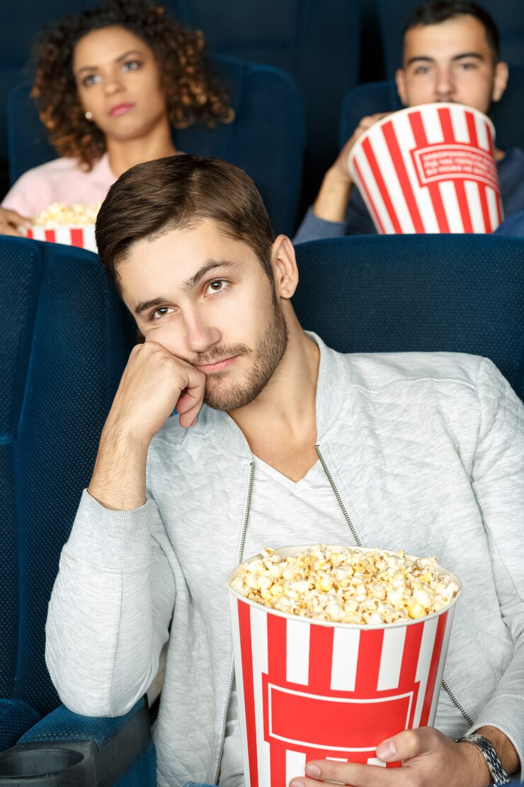 Estremamente annoiato. Colpo verticale di un giovane che sembra annoiato guardando un film al cinema che tiene popcorn