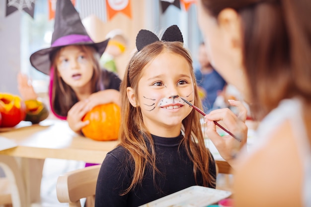 Estremamente eccitato. Ragazza dagli occhi scuri che indossa il costume di Halloween del gatto che si sente estremamente eccitata mentre celebra all'asilo