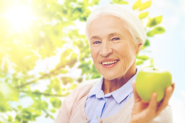 età, alimentazione sana, cibo, dieta e concetto di persone - donna senior sorridente felice con mela verde su sfondo naturale