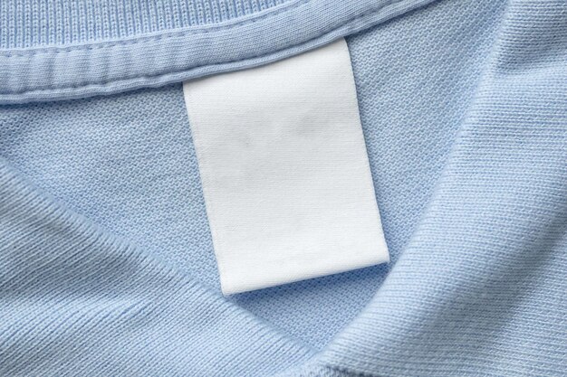 Etichetta bianca di abbigliamento per la lavanderia su sfondo di tessuto blu di camicia