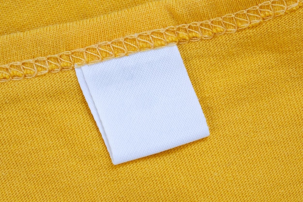 Etichetta bianca vuota dell'etichetta dell'abbigliamento sulla nuova priorità bassa gialla della camicia