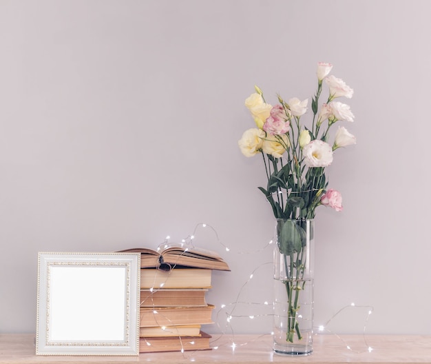 Eustoma bouquet di fiori in un vaso, pila di vecchi libri vintage, cornice per foto bianca e luci di ghirlanda su uno sfondo grigio. Leggere e rilassarsi concetto.