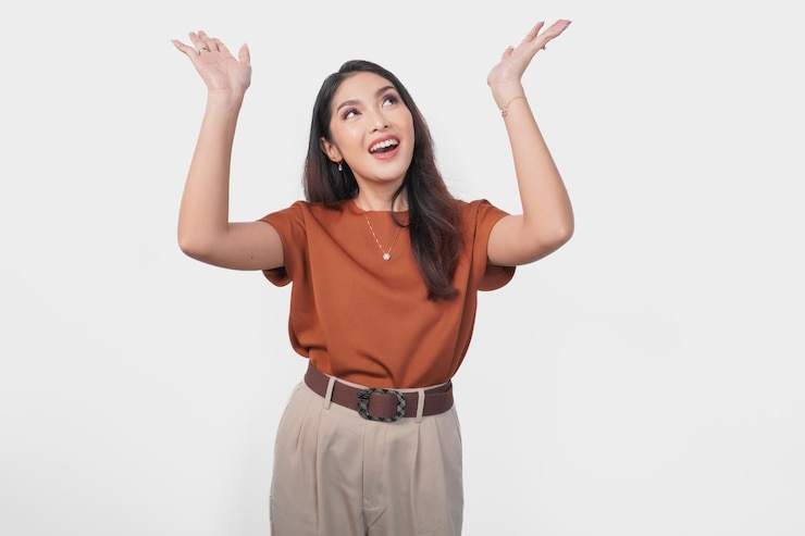 Photo excited asian woman wearing brown shirt pointing to the copy space upside her isolated by white background