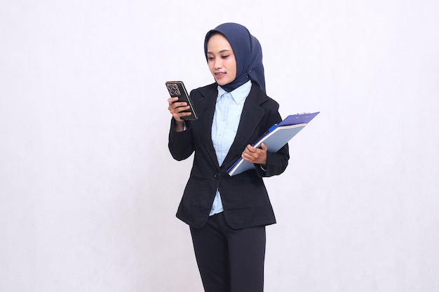 Exclusive indonesia donna d'ufficio che indossa un hijab si trova allegramente a gestire uno smartphone e a portare