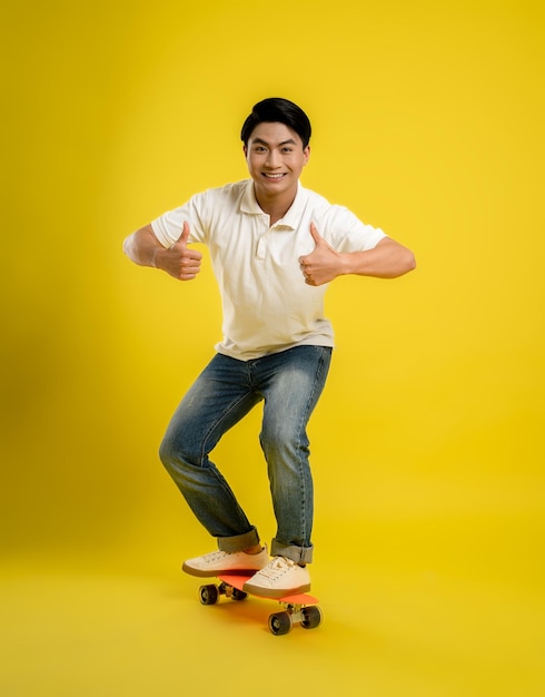 F giovane maschio asiatico che gioca a skateboard su uno sfondo giallo