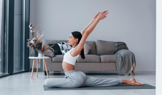 Fa esercizi flessibili La giovane donna con una forma del corpo snella in abbigliamento sportivo ha una giornata di fitness al chiuso a casa
