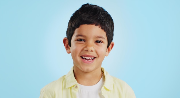 Faccia bambino e sorriso in studio per benessere e fiducia su uno sfondo blu con mentalità positiva Ritratto bambino e felicità con moda casual espressione gioiosa e rilassata sul mockup