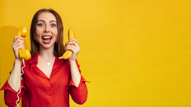 Faccia buffa con una banana e un telefono Una giovane donna con un sorriso tiene una banana in mano