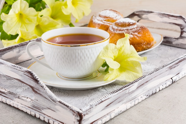 Faccia colazione alla pasticceria e alla tazza danesi di tè sul vassoio d'annata del servizio