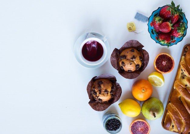 Faccia colazione con caffè e tè con differenti pasticcini e frutti su una tavola di legno bianca