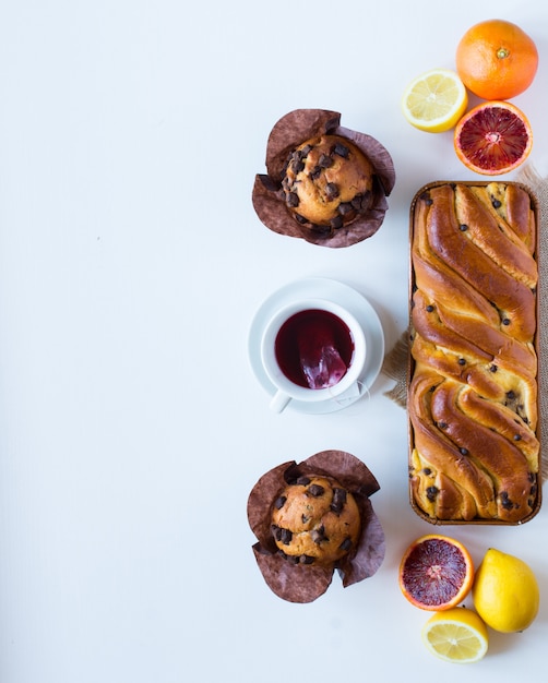 Faccia colazione con caffè e tè con differenti pasticcini e frutti su una tavola di legno bianca